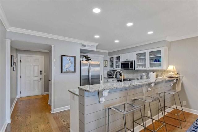 kitchen featuring a kitchen breakfast bar, white cabinetry, light stone counters, kitchen peninsula, and stainless steel appliances