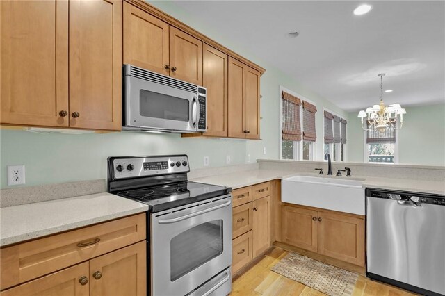 kitchen featuring light stone counters, stainless steel appliances, sink, light hardwood / wood-style flooring, and a chandelier