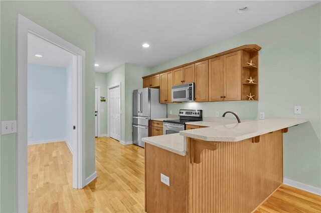 kitchen with light wood-type flooring, kitchen peninsula, and appliances with stainless steel finishes