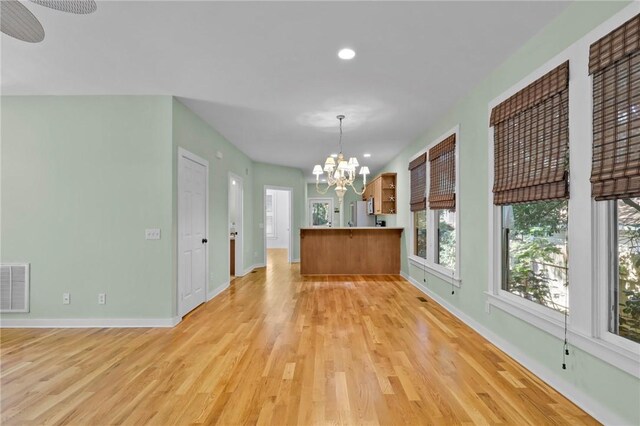 unfurnished dining area featuring ceiling fan with notable chandelier and light wood-type flooring