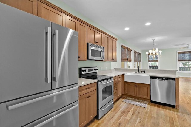 kitchen with kitchen peninsula, appliances with stainless steel finishes, light wood-type flooring, ceiling fan with notable chandelier, and sink