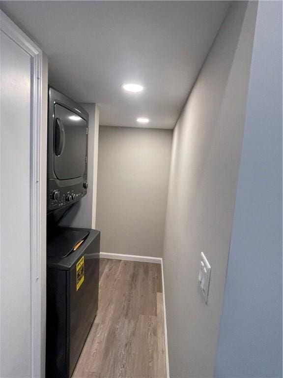 laundry room featuring laundry area, stacked washer / dryer, light wood-style flooring, and baseboards