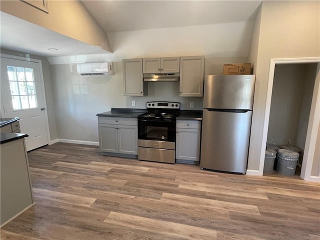 kitchen with under cabinet range hood, an AC wall unit, stainless steel appliances, and dark countertops