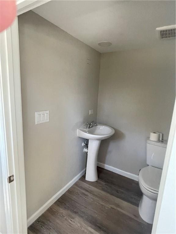 half bath with visible vents, baseboards, toilet, wood finished floors, and a sink