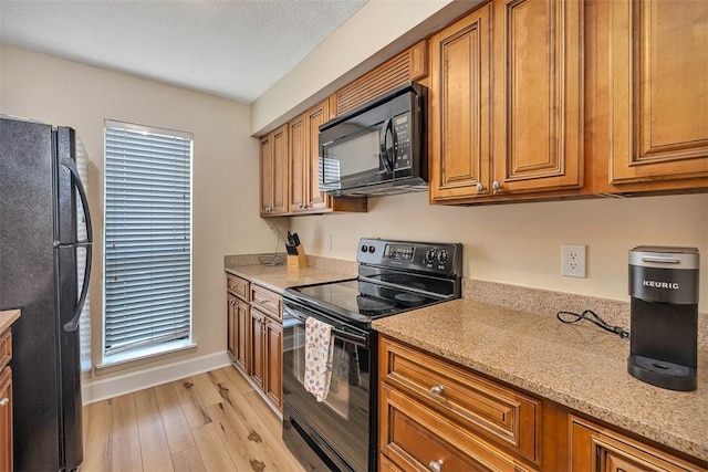 kitchen featuring light stone counters, black appliances, and light hardwood / wood-style floors