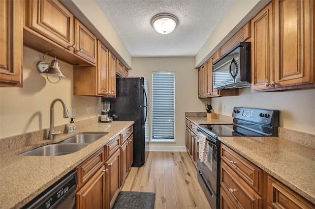 kitchen featuring sink, light stone counters, a textured ceiling, light hardwood / wood-style flooring, and black appliances