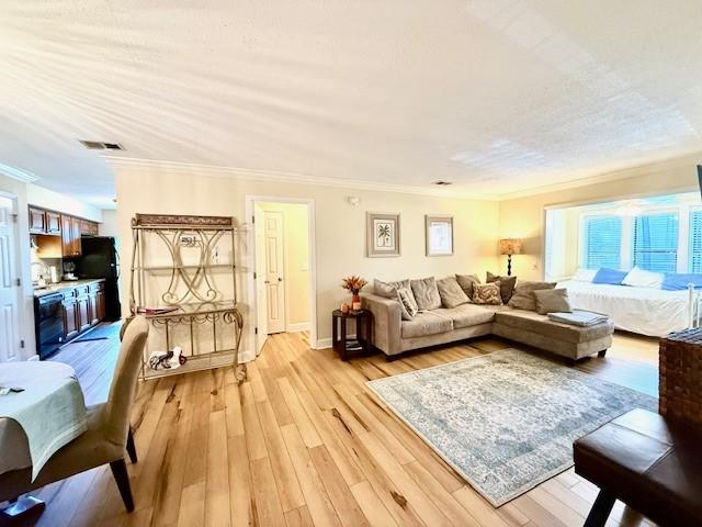 living room featuring a textured ceiling, light hardwood / wood-style floors, ceiling fan, and crown molding