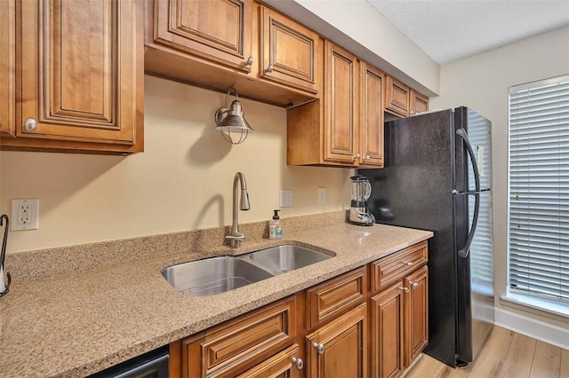 kitchen featuring black refrigerator, sink, light stone counters, a textured ceiling, and light hardwood / wood-style flooring