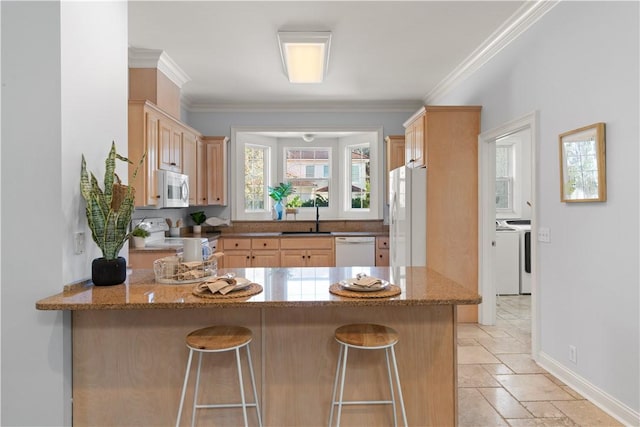 kitchen featuring light stone countertops, white appliances, washing machine and dryer, sink, and kitchen peninsula