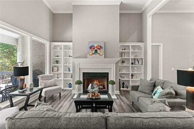 living area featuring a fireplace with flush hearth, ornamental molding, wood finished floors, and a towering ceiling