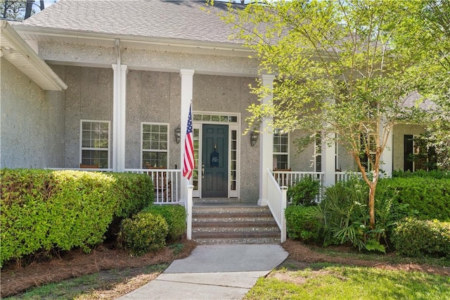 property entrance with covered porch, roof with shingles, and stucco siding