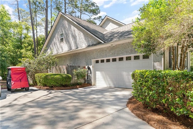 view of side of home with driveway, a garage, fence, a shingled roof, and stucco siding