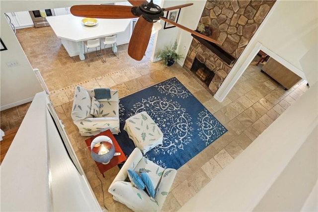 living area featuring ceiling fan, a stone fireplace, and baseboards