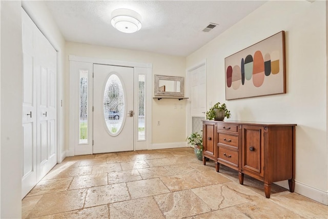 entryway with baseboards, a textured ceiling, visible vents, and stone tile floors