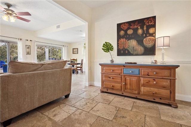 living area with baseboards, visible vents, a ceiling fan, wainscoting, and stone tile flooring