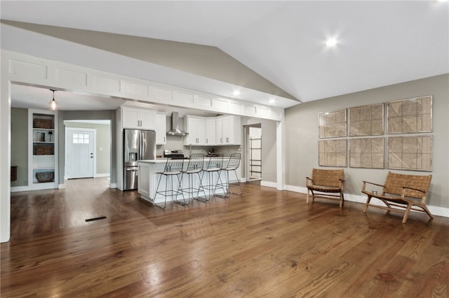 kitchen featuring white cabinetry, stainless steel fridge, a kitchen breakfast bar, dark wood-type flooring, and wall chimney exhaust hood