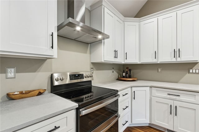 kitchen with wall chimney range hood, vaulted ceiling, white cabinets, and range with two ovens