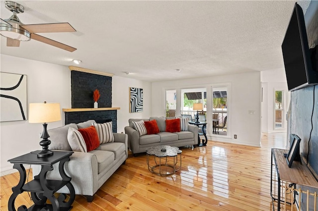 living area featuring a textured ceiling, baseboards, light wood finished floors, and ceiling fan