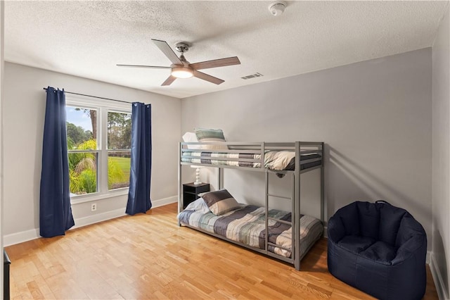 bedroom featuring visible vents, a textured ceiling, baseboards, and wood finished floors