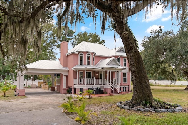 victorian home with a front lawn, covered porch, a chimney, metal roof, and driveway