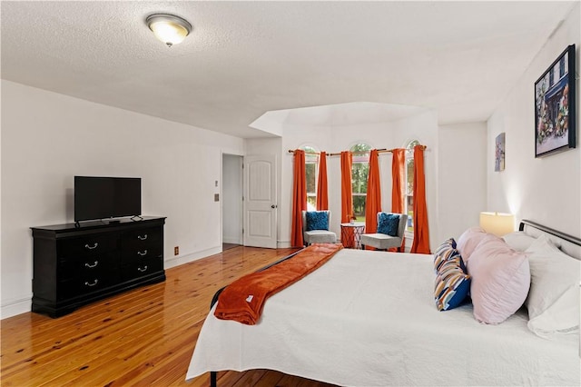 bedroom featuring a textured ceiling, baseboards, and wood finished floors