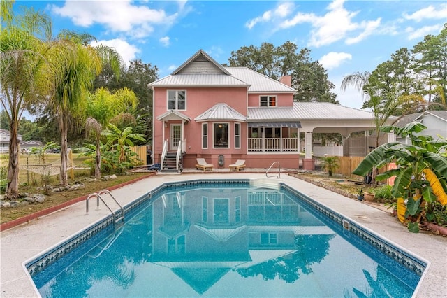 rear view of property with entry steps, an outdoor pool, metal roof, a chimney, and a patio area