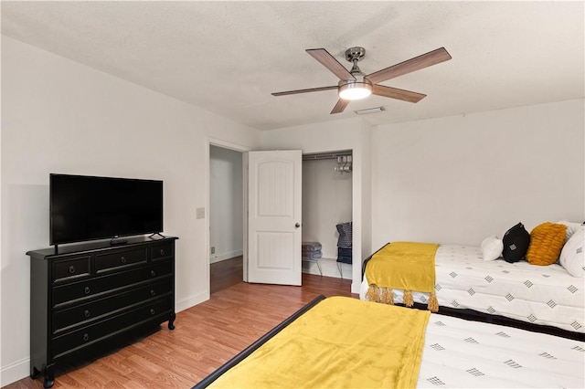 bedroom with wood finished floors, visible vents, baseboards, ceiling fan, and a closet