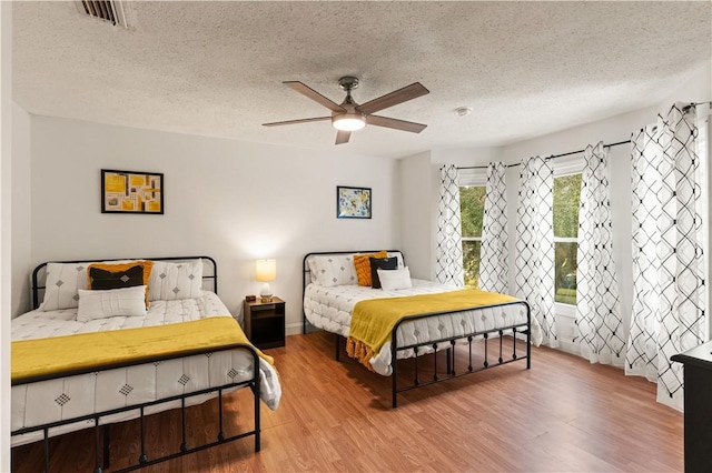 bedroom with ceiling fan, wood finished floors, visible vents, and a textured ceiling