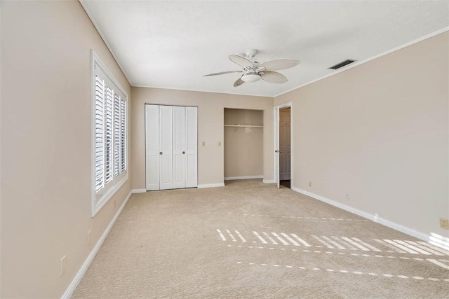 unfurnished bedroom with ceiling fan, light colored carpet, and multiple closets