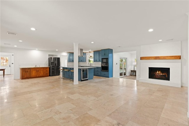 kitchen with a kitchen bar, blue cabinetry, black appliances, open floor plan, and recessed lighting