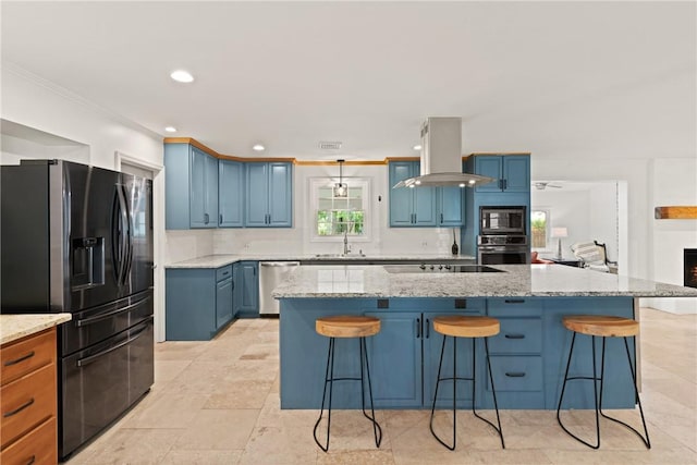 kitchen featuring light stone countertops, a sink, blue cabinetry, island range hood, and black appliances