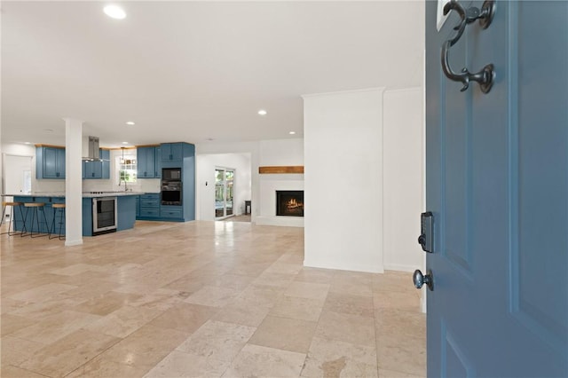 unfurnished living room featuring recessed lighting, a lit fireplace, a sink, and wine cooler