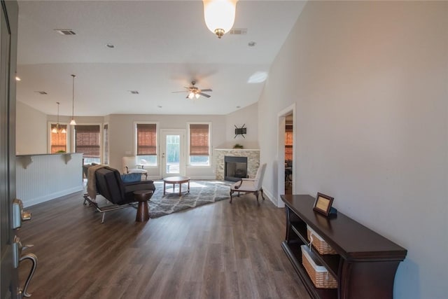 living room featuring a stone fireplace, dark wood-type flooring, and ceiling fan