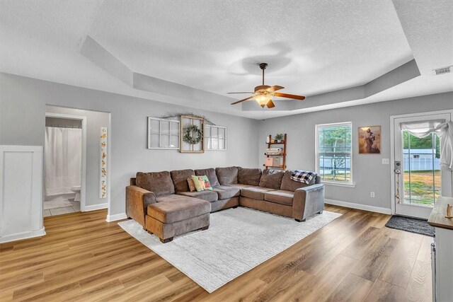 living room with a textured ceiling, a tray ceiling, light hardwood / wood-style flooring, and ceiling fan