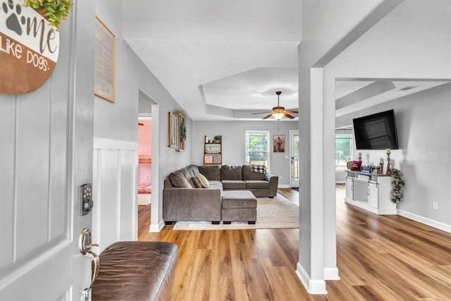 living room featuring a raised ceiling, ceiling fan, and light hardwood / wood-style flooring