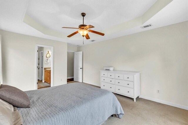 carpeted bedroom with a raised ceiling, connected bathroom, and ceiling fan