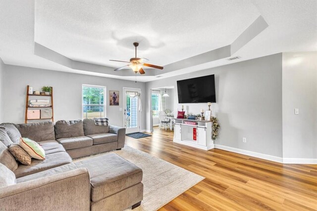 living room featuring a textured ceiling, light wood-type flooring, a tray ceiling, and ceiling fan