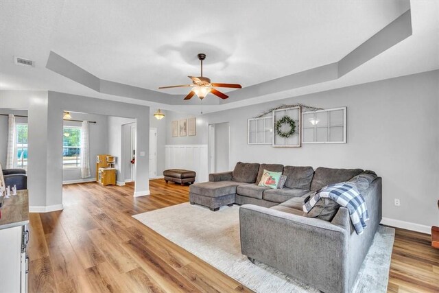 living room with hardwood / wood-style floors, ceiling fan, and a raised ceiling