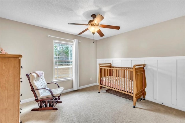 carpeted bedroom with a crib, a textured ceiling, and ceiling fan