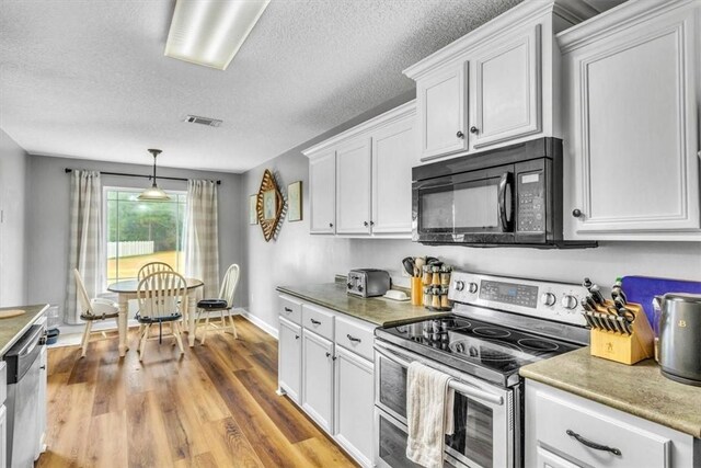 kitchen with pendant lighting, white cabinets, a textured ceiling, appliances with stainless steel finishes, and light hardwood / wood-style floors