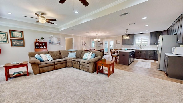 living room with ceiling fan with notable chandelier, sink, crown molding, a tray ceiling, and light hardwood / wood-style floors
