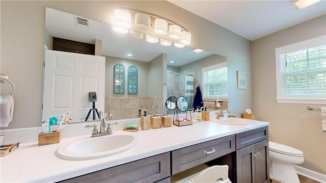 bathroom featuring toilet, plenty of natural light, vanity, and walk in shower