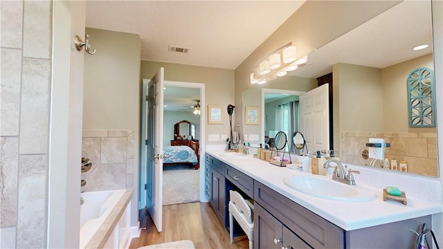 bathroom featuring vanity, a textured ceiling, ceiling fan, wood-type flooring, and a relaxing tiled tub