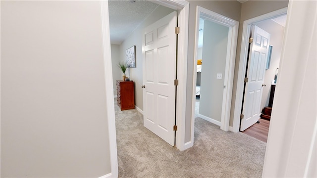 corridor with light carpet and a textured ceiling
