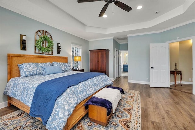 bedroom featuring ceiling fan, connected bathroom, a tray ceiling, and crown molding