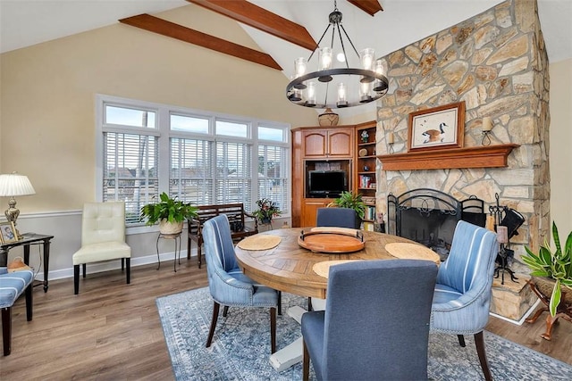 dining space featuring a stone fireplace, a notable chandelier, high vaulted ceiling, light hardwood / wood-style flooring, and beam ceiling