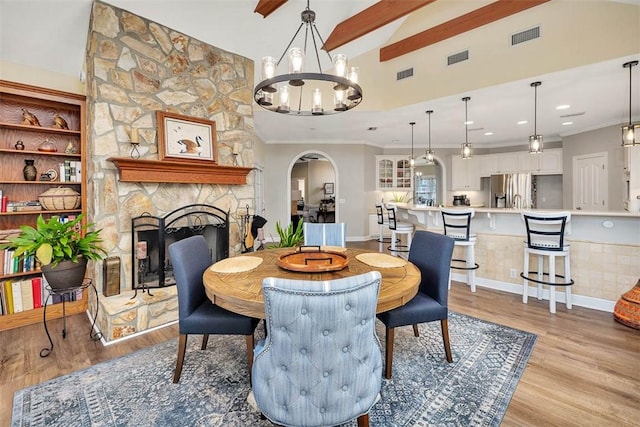 dining area with a towering ceiling, beam ceiling, a fireplace, a notable chandelier, and light hardwood / wood-style floors