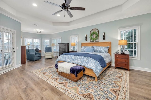 bedroom featuring hardwood / wood-style flooring, a raised ceiling, access to outside, ceiling fan, and multiple windows