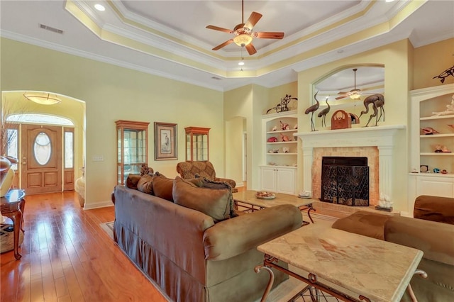 living area with a tray ceiling, hardwood / wood-style flooring, visible vents, and built in features