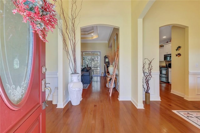 entrance foyer with arched walkways, ornamental molding, a raised ceiling, and light wood-style floors